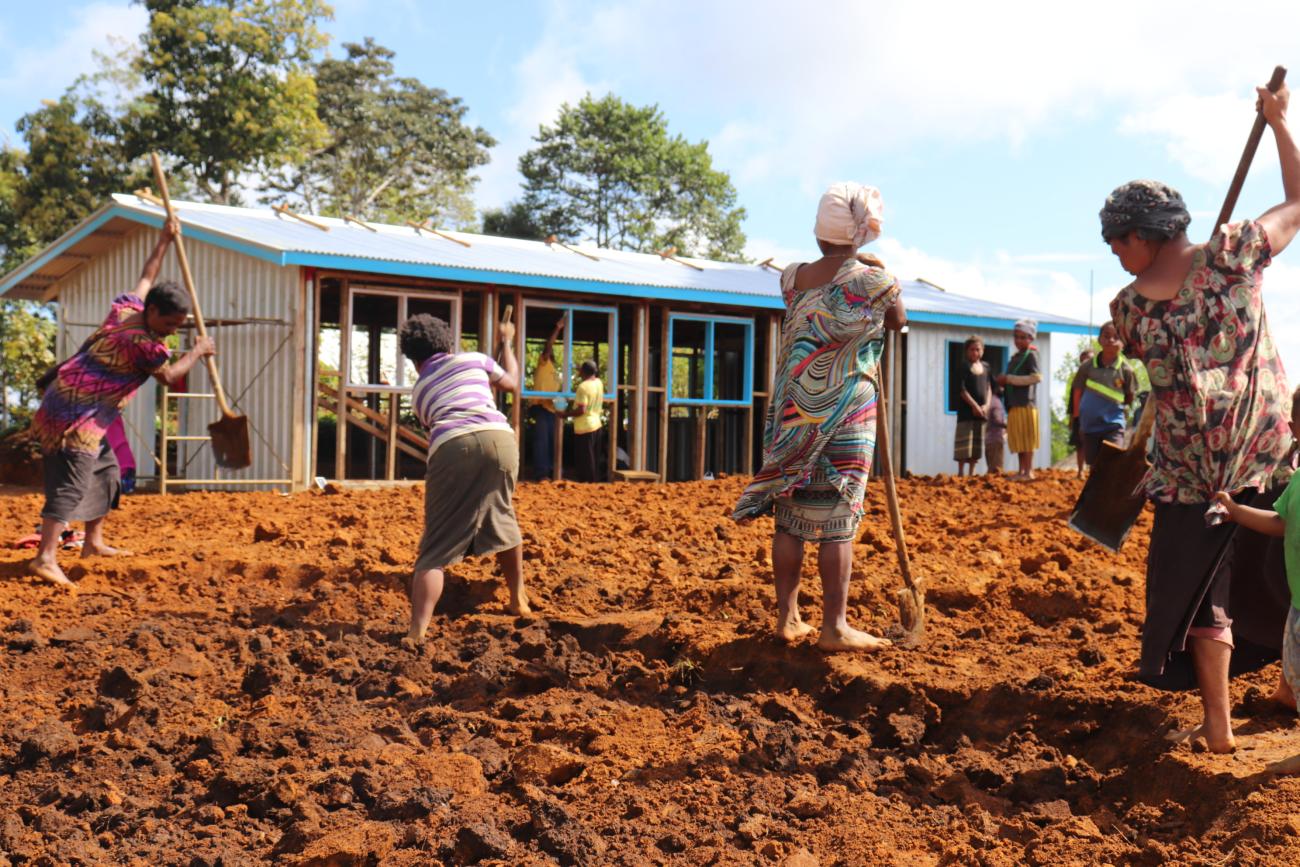 Women digging in field to prepare for building construction. 